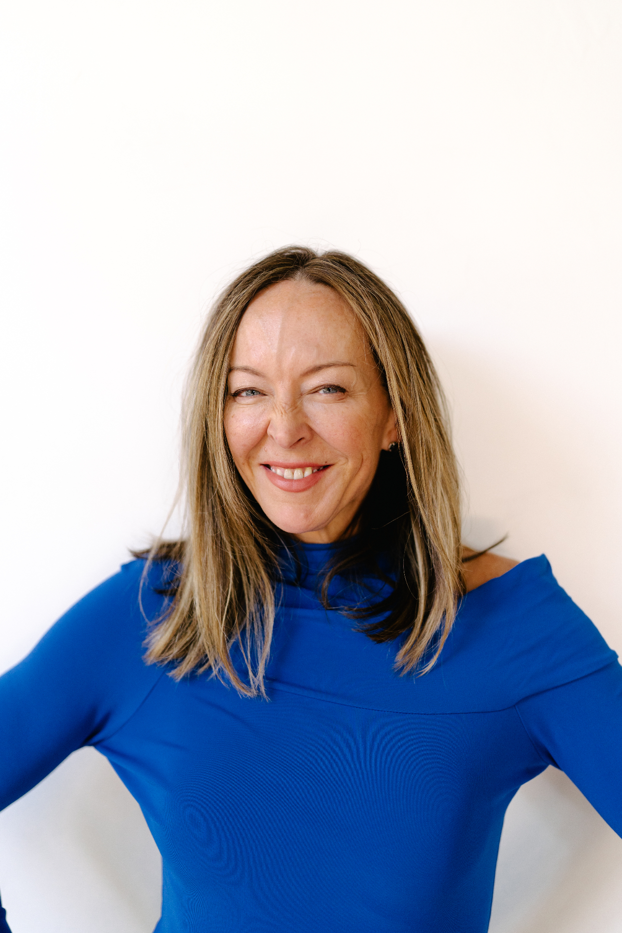 Anese Cavanaugh smiling warmly in a bright blue top against a white backdrop